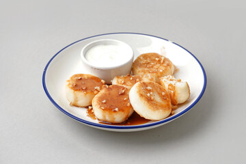 Plate of tasty cottage cheese pancakes with sour cream on light background