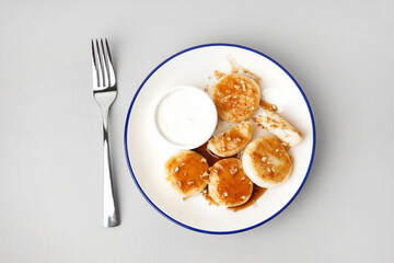 Plate of tasty cottage cheese pancakes with sour cream on light background