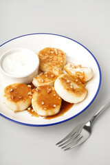 Plate of tasty cottage cheese pancakes with sour cream on light background, closeup