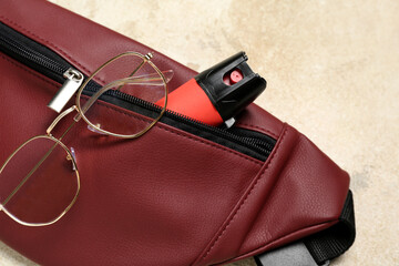 Bag with pepper spray and eyeglasses on grunge background, closeup