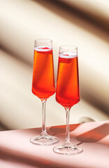Rossini summer alcoholic cocktail drink with sparkling wine or prosecco, strawberry puree and ice in champagne glasses. Beige pink vanilla background, hard light, shadow pattern