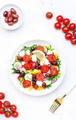 Greek salad with feta cheese, kalamata olives, cherry tomato, yellow paprika, cucumber and onion, healthy mediterranean diet food, low calories eating. White table background, top view