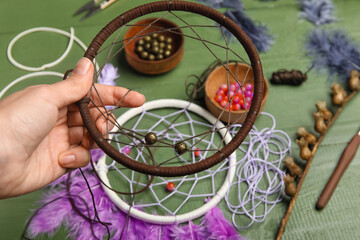 Woman making dream catcher on green wooden background, closeup