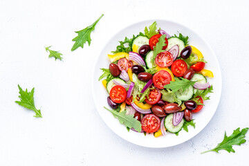 Vegan greek salad with kalamata olives, cherry tomato, yellow paprika, cucumber and red onion, healthy mediterranean diet food, low calories eating. White table background, top view