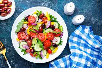 Vegan greek salad with kalamata olives, red tomato, yellow paprika, cucumber and onion, healthy mediterranean diet food, low calories eating. Blue stone background, top view