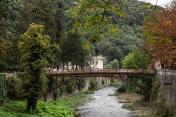 Fototapeta na wymiar Panorama of the river Cerna in Baile Herculane, with te podul de fonta, or cast iron bridge, a rusty vintage bridge, in the middle of the mountains in the romanian countryside.