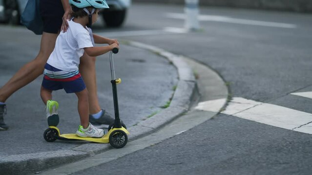 Mother and child crossing street on crosswalk zebra lines. Parent protecting little boy riding scooter with helmet in city street