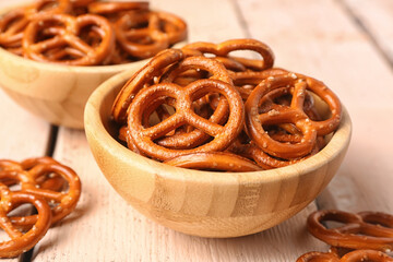 Bowls of tasty pretzels on light wooden background, closeup