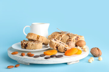 Board with delicious biscotti cookies, nuts, chocolate and dried apricots on blue background