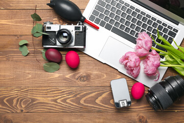 Photographer's equipment with laptop, Easter eggs and flowers on wooden background