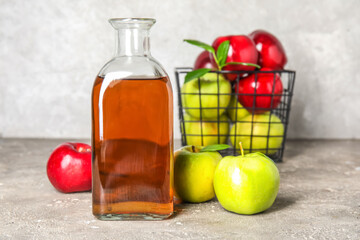 Glass bottle of fresh apple cider vinegar and fruits on grey grunge table