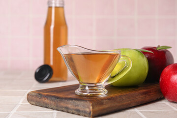 Gravy boat with fresh apple cider vinegar and fruits on pink tile table