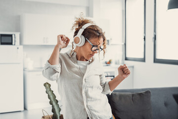Overjoyed millennial girl wearing headphones have fun moving listening to music relax in living room, happy young woman in earphones dance enjoy leisure weekend at home, stress free concept.