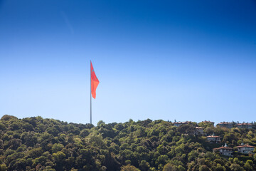 Panorama of a hill with wood, nature and forest with Turkish flag floating in the air in front of a blue sky in istanbul. Also called Turk Bayragi, the flag of turkey, red with a white crescent, is th