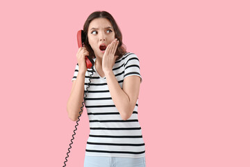 Shocked young woman with phone receiver on pink background