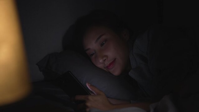 Young Asian woman using a smartphone in her bed at night.