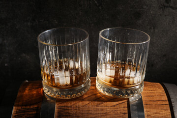 Glasses of cold whiskey on wooden barrel against dark background