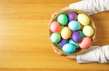 A girl, five years old, holding a wooden basket with many colored Easter eggs in her hands.