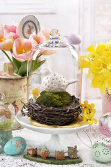 Easter table in vintage style with ceramic bird in a nest under glass cloche