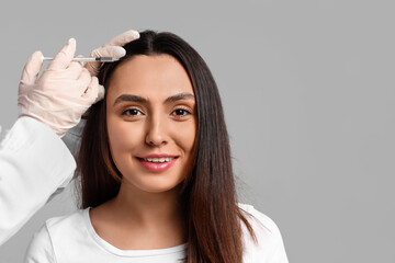 Woman with hair loss problem receiving injection on grey background