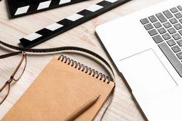 Notebook with film, movie clapper and laptop on light wooden background