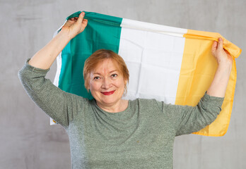 Happy mature lady standing proudly holding flag of ireland