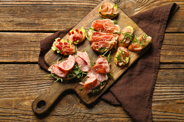 Board of tasty bruschettas with ham on wooden background