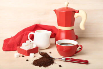 Spoon of coffee powder, sugar, milk jug, cup and maker on light wooden table