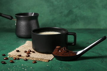 Spoon of coffee powder with beans and cup on green table, closeup