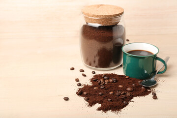 Spoon of coffee powder, beans, cup and jar on light wooden table