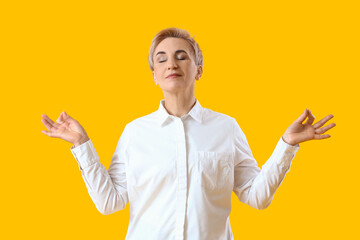 Mature woman meditating on yellow background