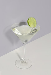 Glass of martini with lime on light background