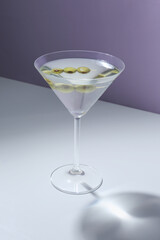 Glass of martini with olives on color background