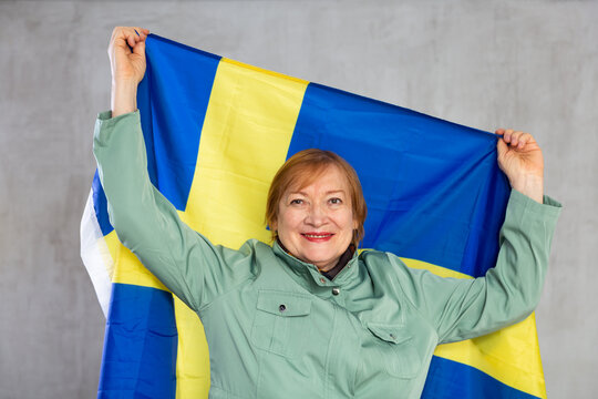 Happy mature lady standing proudly holding flag of sweden