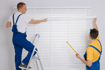 Workers in uniforms installing horizontal window blinds indoors