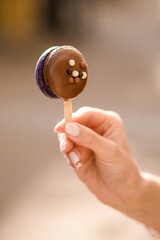 female hand holding delicious sweet macaron in chocolate icing on a stick