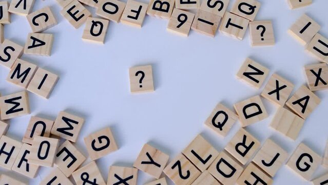 female hand close-up holds wooden alphabet blocks, makes up question marks from wooden letters on white background, dyslexia awareness, literacy problems, idea, human brain development concept