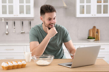 Happy man learning to cook with online video on laptop at table in kitchen. Time for hobby