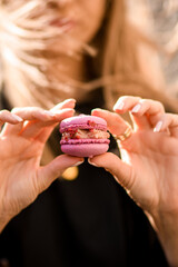 Selective focus on delicious pink macaron in female hands on blurred background