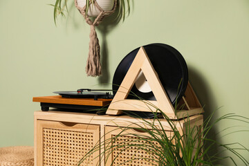 Vinyl records and player on wooden cabinet near light green wall