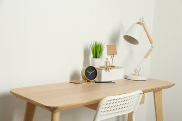 Comfortable workplace with wooden desk near white wall
