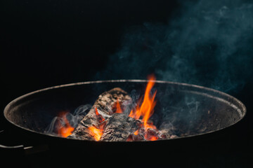 Firewood burns in a round barbecue at night. Dark background. Preparing to cook food on the grill.