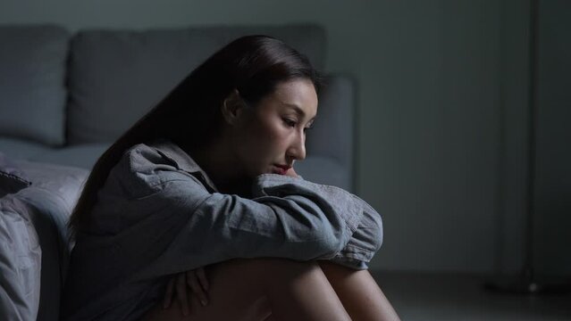 Young Asian woman sitting on floor at home feeling sad tired and worried suffering depression in mental health.