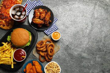 French fries, burger and other fast food on gray textured table, flat lay with space for text