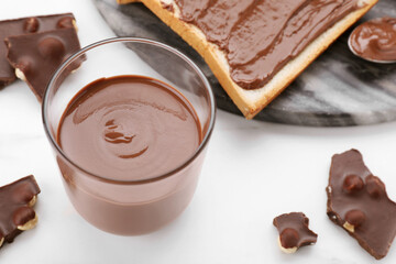 Tasty breakfast. Glass with sweet paste and chocolate pieces on white table, closeup