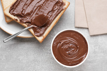 Tasty breakfast. Toast with chocolate paste served on grey textured table, flat lay