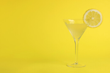 Martini glass of refreshing cocktail with lemon slice on yellow background, space for text