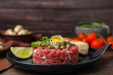 Tasty beef steak tartare served with quail egg and other accompaniments on wooden table