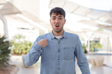 Fototapeta premium young handsome man looking shocked and surprised with mouth wide open, pointing to self