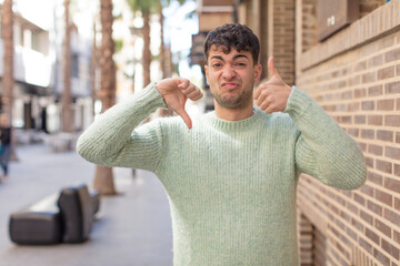 young handsome man feeling confused, clueless and unsure, weighting the good and bad in different...